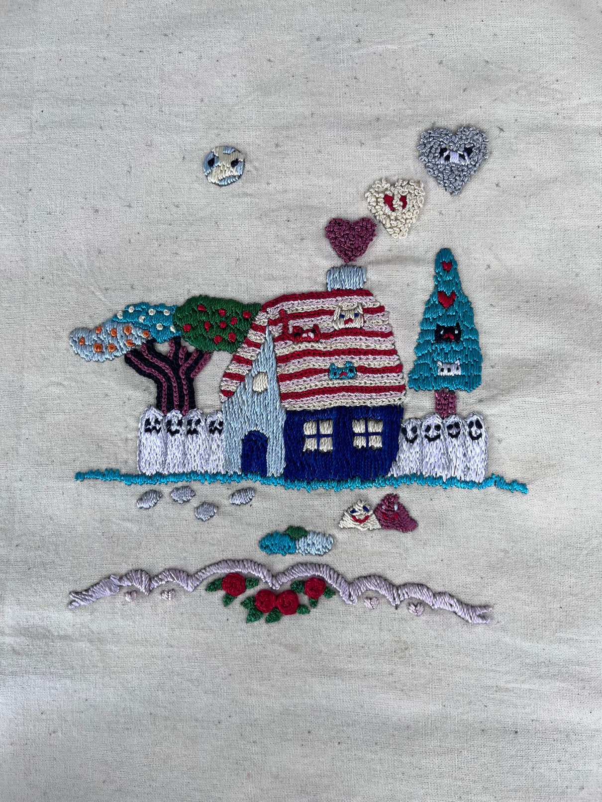 Proyecto de bordado Crewel ilustrativo con casa, árboles, corazones, flores y detalles bordados sobre tejido